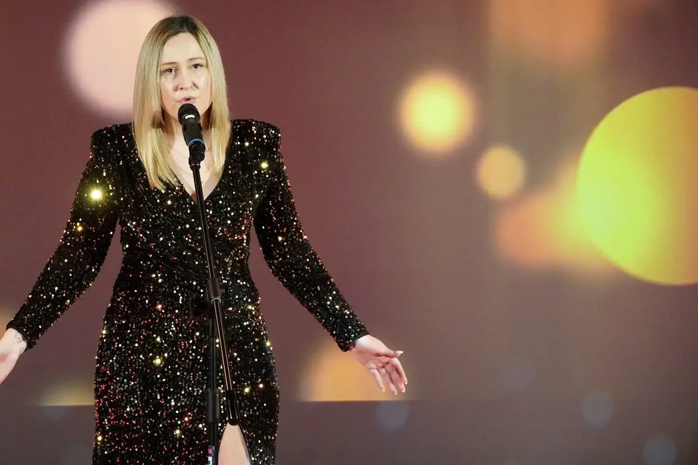 Gabriela Krzeszowiak śpiewa na scenie w cekinowej sukni, w tle światła sceniczne